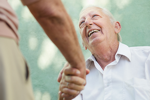 Elderly man in white button down shirt looking up and man he's shaking hands with