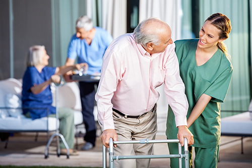 Young nurse in green scrubs assisting elderly man with walker