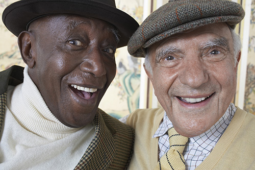 Close up of two elderly gentlemen smiling both wearing hats